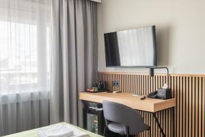 a hotel room with a desk with a television on the wall at AIRINN Vilnius Airport Hotel RENOVATED 2025 in Vilnius