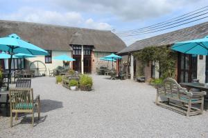 a patio with chairs and umbrellas in front of a building at Berehayes Cottages in Whitchurch Canonicorum +7 photos