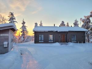 a house covered in snow with the sun setting behind it at The Copper Nest by Hilla Villas in Saariselka