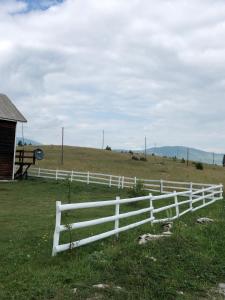 a white fence in a field next to a barn at brown bear lodge in Žabljak