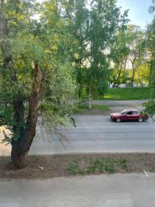 a red car driving down a street next to a tree at Квартира на Протозанова 39 in Ustʼ-Kamenogorsk