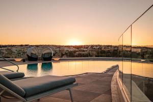 a pool on the roof of a building with the sunset at Hyatt Regency Malta in St. Julianʼs