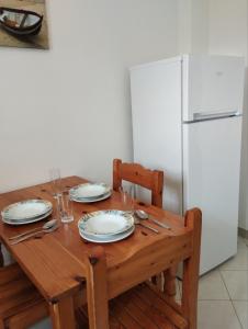 a wooden table with plates and glasses and a refrigerator at Nikos Apartments 2 in Kavos