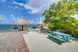 a picnic table and straw umbrellas on a beach at Walk to Beach Florida Keys Gem with Ocean Views in Layton