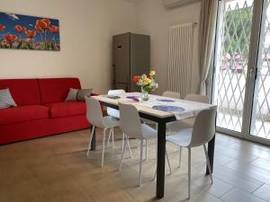 a dining room table with white chairs and a red couch at Le Casine di Cervia in Cervia