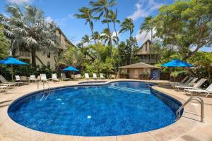 a swimming pool with chairs and blue umbrellas at Tropical Treehouse Near the Beach in Koloa