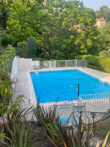 Clim Jardin et parking privé -piscine tennis et Park Vue mer في جراس: حوض سباحة كبير باللون الأزرق مع سياج أبيض حوله