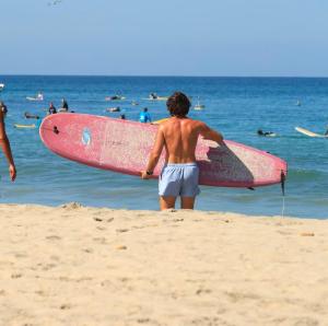 a man standing on the beach holding a pink surfboard at Casa Villa Noa in Puerto Escondido