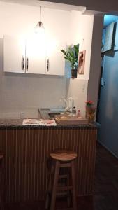 Una cocina con gabinetes blancos y una barra con un taburete. en kitnet aconchegante Miguel Pereira, en Miguel Pereira