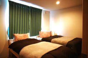 a bedroom with two beds and a window with green curtains at Hana Hostel Fujisan Apartment in Fujiyoshida
