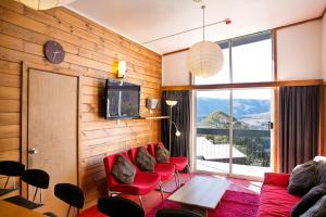 a living room with red chairs and a large window at Kilimanjaro Alpine Apartments in Falls Creek