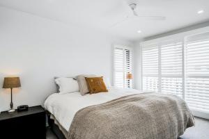 a bedroom with a bed with white walls and windows at Sanctuary Spaces - Lomani Six in Byron Bay +27 photos
