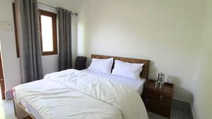 a bedroom with a bed with white sheets and a window at Shree Nath Ji in Barkot