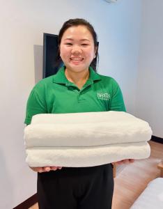 a woman holding three towels in a room at Nantra de Comfort in Bangkok