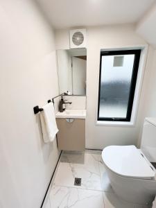 a white bathroom with a toilet and a window at Brand New 2 Bed Near CBD With Parking in Christchurch +11 photos