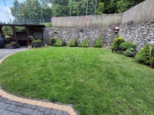 a yard with a stone wall and a dog standing in the grass at Apartament JOANNA in Sanok