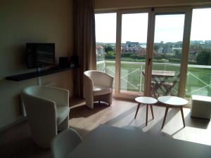 una sala de estar con sillas, mesas y una gran ventana. en Apartment Green Garden Block L, en Middelkerke