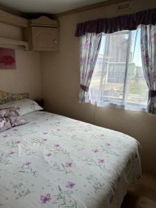 a bedroom with a bed with a floral comforter and a window at 27 Glenfinart Caravan Park in Dunoon +3 photos