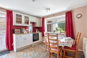 une cuisine avec des rideaux rouges et une table avec des chaises dans l'établissement Riverview Cottage - North East Escapes, à Warkworth