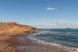 a beach with the ocean and a house on a cliff at Home2Book Bright Retreat with Roof Access in Vecindario