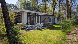 a small cottage with chairs and an umbrella at Boslodge Het Groene Hert met Hottub in Haarle
