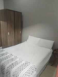 a bed with white sheets and a wooden cabinet at Melee's house in Richards Bay