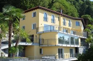un edificio amarillo con balcones y árboles en Casa Serena, 3-Zimmerwohnung-Duplex by HolAp SA, en Brione sopra Minusio