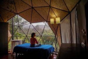 a woman sitting on a bed in a room with a large window at Glamping Bosque del Colibri in Guatavita