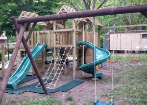 a playground with two swings and a wooden building at Parco Del Lago Glamping And Camping in Anguillara Sabazia