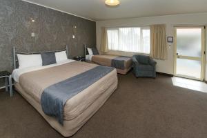 una habitación de hotel con dos camas y una silla en Geneva Motor Lodge, en Rotorua