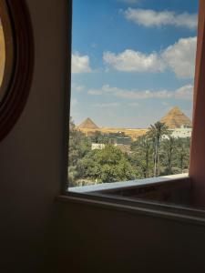 a window with a view of palm trees and mountains at BrassAlmas Pyramids Hotel in Cairo