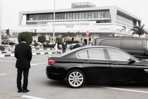 Un homme debout à côté d'une voiture noire dans un parking dans l'établissement Hotel Florença, à Talatona