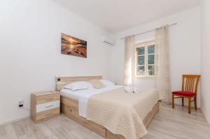 a white bedroom with a bed and a red chair at Apartment Kokic in Zastražišće
