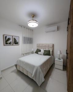 a white bedroom with a large bed and a lamp at Escapada perfecta, apartamento frente al mar in San Felipe de Puerto Plata