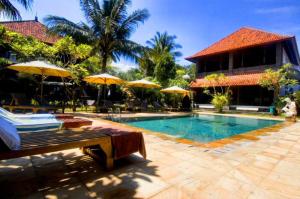 una piscina con sillas y sombrillas junto a un edificio en Puri Rai Hotel en Padangbai