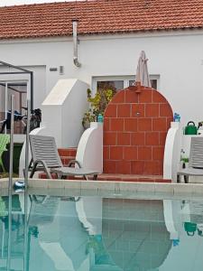 a swimming pool with two chairs and a red brick wall at Casinhas Vale de Mouro in Melides