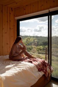 a woman sitting on a bed in front of a window at TEKOÁ - Cabana Pitanga - Barreiro, Araxá in Araxá