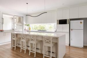 a white kitchen with a large white island with stools at Large Premium Family Getaway with Centralised Heating in Shepparton