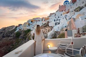 a woman standing on a balcony looking at a cliff at Kyrkos Collection in Fira +29 photos
