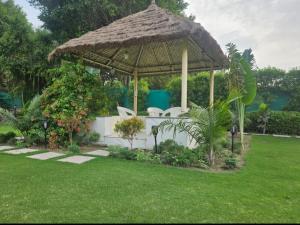 Un cenador con sillas blancas y una sombrilla de paja. en Shree Krishna Dham 3BHK Villa with Private Pool and Lush Garden in Noida sector 135, en Noida