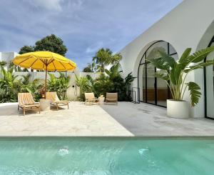 a pool with chairs and an umbrella next to a house at Dolce x The Young Villas in Uluwatu