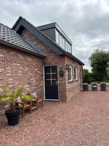 a brick house with a black door and two benches at B&B 'Op Eemdijk' in Eemdijk