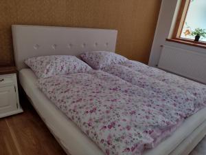 Una cama deshecha con cabecero blanco y flores rosas. en Bara ház, en Tvrdošovce