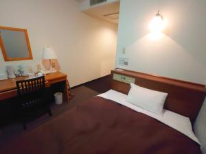 a room with a bed and a desk and a lamp at Garden Hotel Matsumoto in Matsumoto