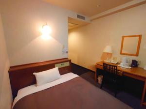a room with a bed and a desk and a lamp at Garden Hotel Matsumoto in Matsumoto