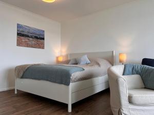 a white bedroom with a bed and a chair at Baltic Sea View in Fehmarn