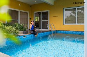 a woman sitting by a swimming pool talking on a cell phone at EKOSTAY - Casa Den in Igatpuri