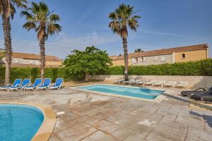 una piscina con sillas y palmeras en Résidence Odalys Le Grand Bleu, en Vendres-Plage