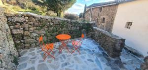Una mesa y sillas naranjas junto a un muro de piedra. en Calme, détente, balades, nature en Cévennes, en Cros