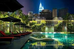 una piscina con sedie e ombrelloni e una città di notte di E&O Residences Kuala Lumpur a Kuala Lumpur